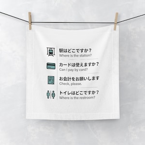 May include: A white square towel featuring four rows of Japanese text paired with English translations and corresponding icons: a train for station location, a credit card for payment, a receipt for the check, and restroom symbols.