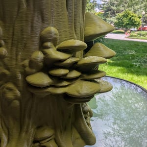 May include: An olive green 3D printed planter shaped like a tree stump with a cluster of textured mushrooms growing from the side. The surface of the stump features vertical ridges and organic details, while the mushrooms have layered caps.
