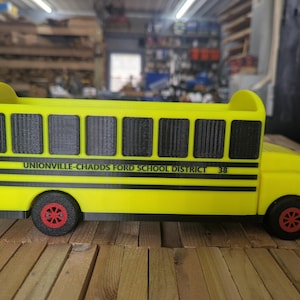 May include: A bright yellow school bus desk organizer with black windows and trim. The side features the text UNIONVILLE-CHADDS FORD SCHOOL DISTRICT and the number 38. The bus has red wheels with black tires and an open top for storage.