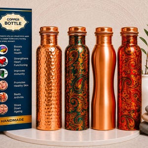 Puede incluir: Cuatro botellas de cobre junto a una caja azul con la etiqueta COPPER BOTTLE. La primera botella tiene una textura martillada, la segunda presenta un patrón de cachemira verde y dorado, la tercera es de cobre pulido y la cuarta tiene un diseño rojo.