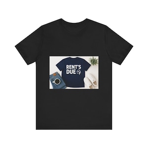 May include: A black short-sleeve t-shirt featuring a centered graphic of a navy blue t-shirt with the white text RENT'S DUE and a small house icon with a key. The graphic also displays blue jeans, a cup of coffee, white sneakers, and a small plant.