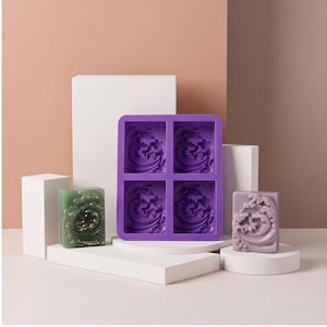 May include: A purple silicone mold featuring four square cavities with a raised wave design. Beside the mold are two rectangular soap bars, one in translucent green with gold glitter and one in solid light purple, both displaying a wave pattern.