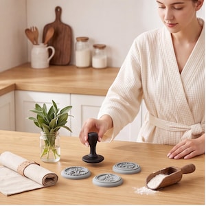 Peut inclure: Un tampon à biscuits avec un manche noir et trois disques interchangeables en silicone gris clair, présentant des motifs en relief d'un bonhomme en pain d'épices, d'un sapin de Noël et d'un cadeau, avec une pelle à farine en bois.