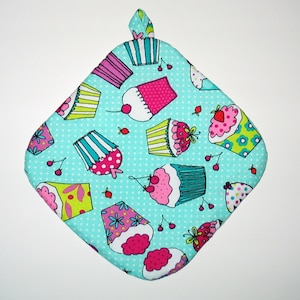 May include: A turquoise blue pot holder with a white polka dot pattern and a colorful cupcake design. The cupcakes are pink, green, yellow, and blue with white frosting and sprinkles.