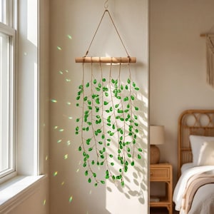Peut inclure: Une décoration murale suspendue composée d'une tige en bois horizontale retenue par une ficelle. Plusieurs brins de fil métallique pendent de la tige, ornés de nombreuses petites perles en verre vert en forme de goutte d'eau.