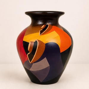 Puede incluir: Un jarrón de cerámica con cuello ancho y cuerpo redondeado, con un acabado liso. La superficie está decorada con formas geométricas en colores vibrantes que incluyen naranja, rojo, amarillo, morado y negro, creando un patrón abstracto audaz.