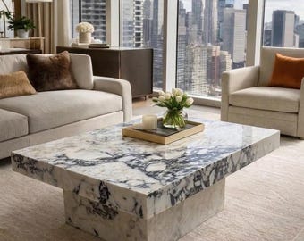 May include: A rectangular coffee table featuring a polished white and dark grey marble top with a matching block base. The table surface holds a rectangular wooden tray containing a clear glass vase filled with white tulips and a white candle.