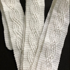 May include: Three white crocheted trim pieces with a diamond pattern. The trim is made of a soft, delicate yarn and has a slightly textured surface.