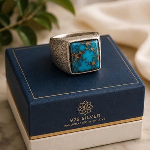 May include: A silver ring with a textured band and a square turquoise stone featuring copper-coloured veining. The ring rests on a navy blue box with gold trim, displaying the text 925 SILVER HANDCRAFTED WITH LOVE and a floral logo.
