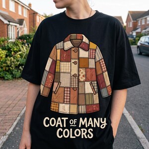 Può includere: Una t-shirt nera con un'illustrazione grafica di un cappotto patchwork realizzato con vari quadrati di tessuto marrone, beige e rosso. Il cappotto ha un colletto e quattro bottoni. Sotto il cappotto, il testo recita COAT OF MANY COLORS.