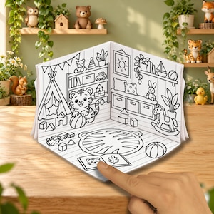 Könnte beinhalten: Ein dreidimensionales Papier-Malbastelset mit einer schwarz-weißen Strichzeichnung eines Kinderzimmers. Die Szene zeigt einen Tiger, ein Tipi, ein Schaukelpferd, einen Teppich und verschiedene Spielzeuge. Ein Finger zeigt auf ein offenes Buch.