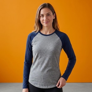 May include: A long-sleeve raglan shirt featuring a heather grey torso and solid navy blue sleeves. The garment has a round neckline and a curved hemline, constructed with a classic baseball-style design that provides full arm coverage.