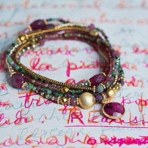 Puede incluir: Un brazalete de m&uacute;ltiples hilos con cuentas doradas, piedras preciosas rosas y verdes, y un gran colgante de piedra preciosa rosa.
