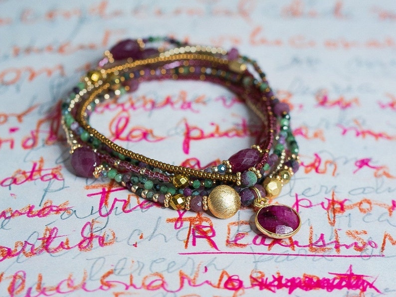 Puede incluir: Un brazalete de m&uacute;ltiples hilos con cuentas doradas, piedras preciosas rosas y verdes, y un gran colgante de piedra preciosa rosa.