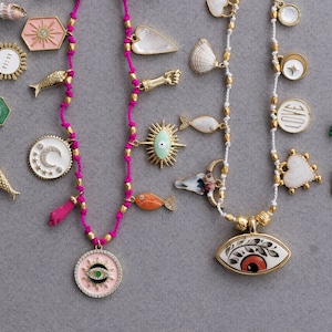 May include: A collection of colorful necklaces with various charms, including fish, hearts, stars, moons, and eyes. The necklaces are made with different colored cords and beads.