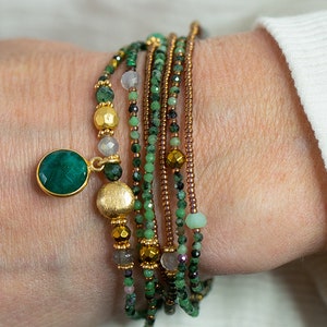 K&ouml;nnte beinhalten: Ein mehrreihiges Armband mit gr&uuml;nen, braunen und goldenen Perlen. Das Armband hat einen gro&szlig;en Anh&auml;nger aus gr&uuml;nem Edelstein.