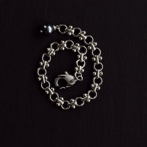 May include: A silver chain bracelet with a dark gray pearl charm and a lobster clasp closure.
