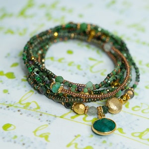 K&ouml;nnte beinhalten: Mehrreihiges Armband mit gr&uuml;nen und goldenen Perlen, mit einem gro&szlig;en gr&uuml;nen Edelstein-Anh&auml;nger.