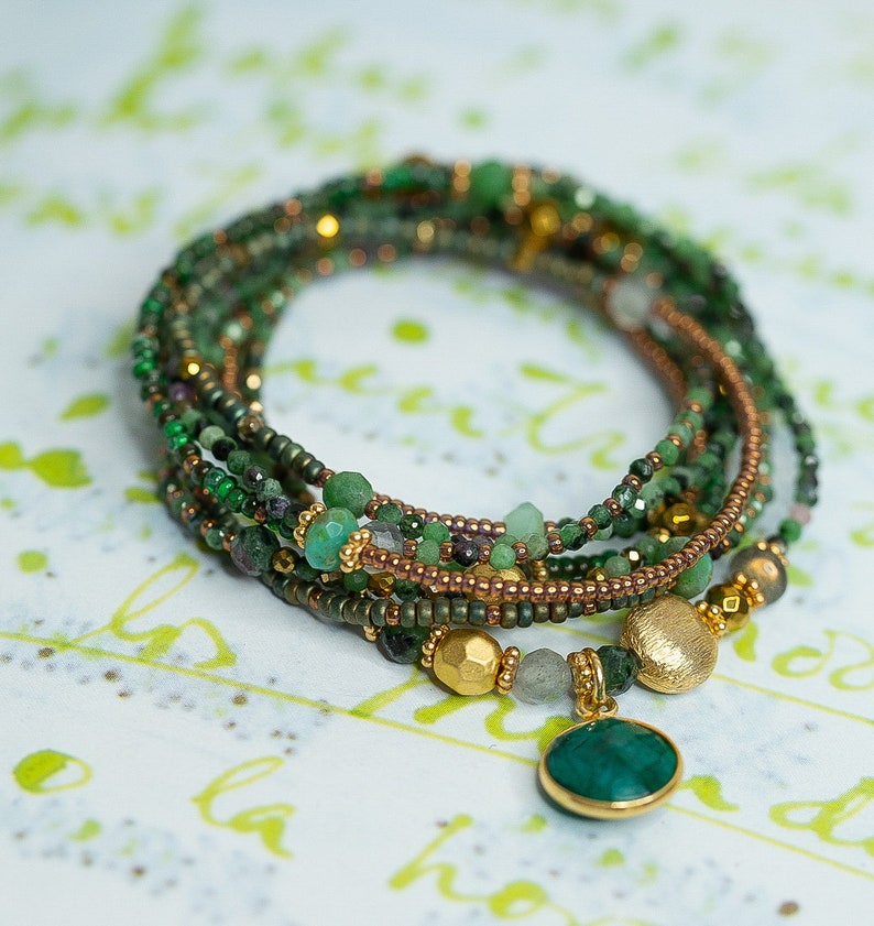 K&ouml;nnte beinhalten: Mehrreihiges Armband mit gr&uuml;nen und goldenen Perlen, mit einem gro&szlig;en gr&uuml;nen Edelstein-Anh&auml;nger.