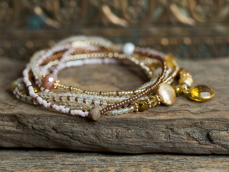 May include: A multi-strand beaded bracelet with a gold charm and a light brown, pink, and clear color scheme.