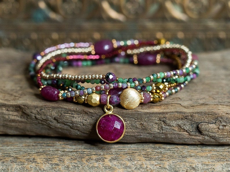 Puede incluir: Pulsera de m&uacute;ltiples hilos con un colgante de oro con una gran piedra de rub&iacute;. La pulsera est&aacute; hecha con peque&ntilde;as cuentas en tonos rosa, verde y dorado.