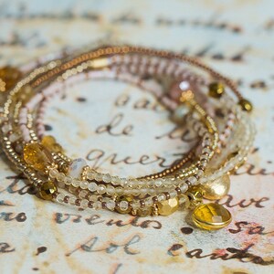 May include: A multi-strand bracelet with gold, brown, and white beads. The bracelet has a gold charm with a clear stone.