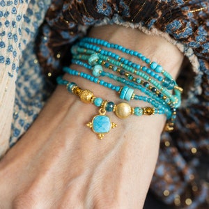 May include: A stack of turquoise and gold beaded bracelets with a turquoise and gold pendant charm.