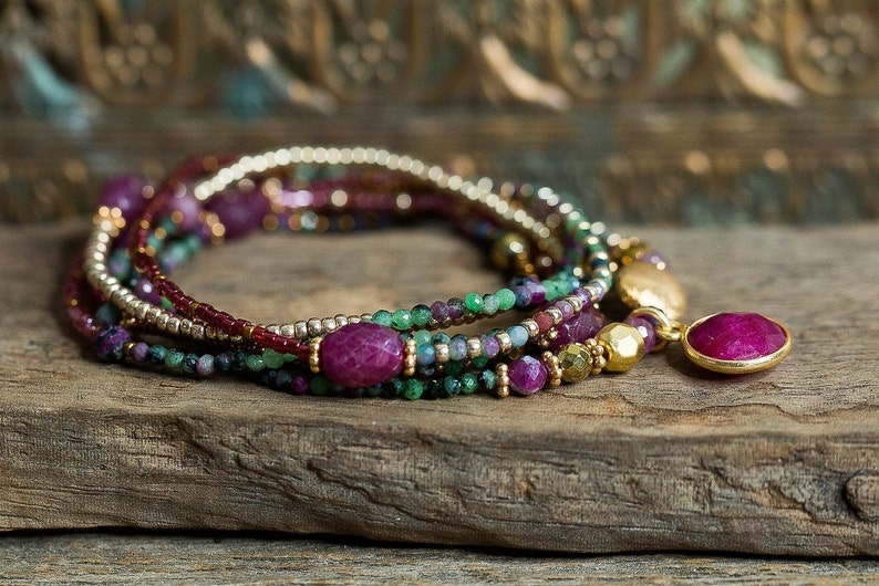 Puede incluir: Un brazalete de m&uacute;ltiples hilos con cuentas rosas, verdes y doradas. El brazalete tiene un gran colgante de piedra preciosa rosa.