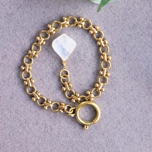 May include: A gold chain bracelet with a white moonstone pendant. The bracelet has a lobster clasp closure.