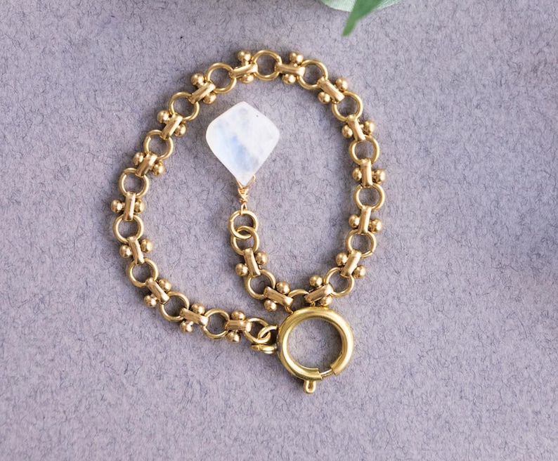 May include: A gold chain bracelet with a white moonstone pendant. The bracelet has a lobster clasp closure.