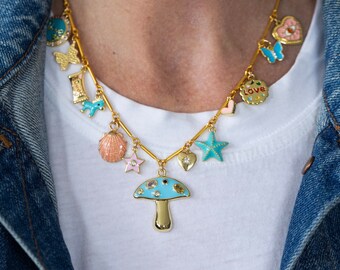 Può includere: Una collana a catena dorata con più ciondoli, tra cui una conchiglia, una stella, un cuore, un fungo, una farfalla e un ciondolo che dice "Love".