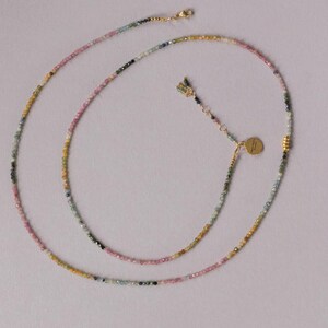 Pu&ograve; includere: Una delicata collana con piccole perline multicolori nei toni del rosa, verde, giallo e nero. La collana ha una chiusura color oro e un piccolo ciondolo rotondo. Le perline sono infilate per creare un design lungo ed elegante.
