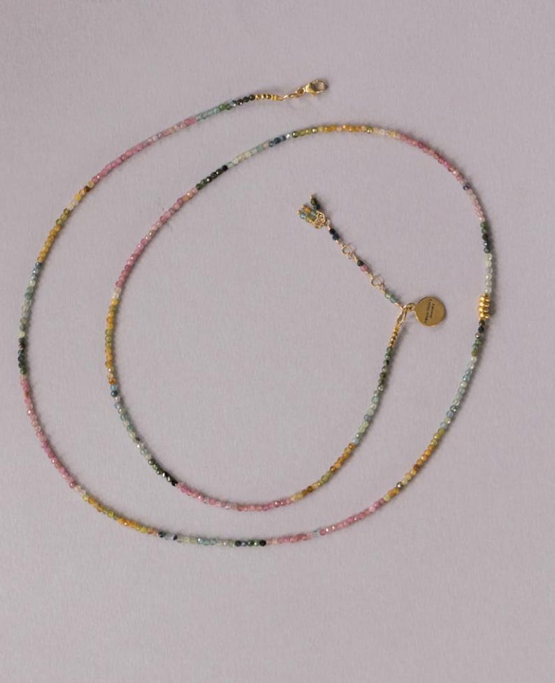 Pu&ograve; includere: Una delicata collana con piccole perline multicolori nei toni del rosa, verde, giallo e nero. La collana ha una chiusura color oro e un piccolo ciondolo rotondo. Le perline sono infilate per creare un design lungo ed elegante.