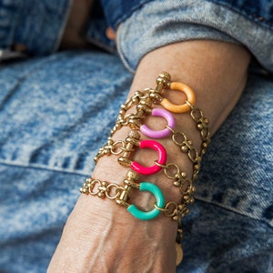 May include: A stack of gold chain bracelets with colorful enamel accents. Each bracelet features a unique color, including turquoise, pink, purple, and orange.