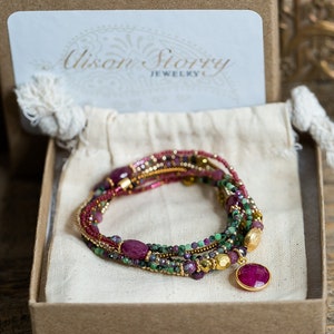 Puede incluir: Un brazalete de m&uacute;ltiples hilos con piedras preciosas rojas y verdes y cuentas doradas. El brazalete tiene un gran colgante de piedra roja.