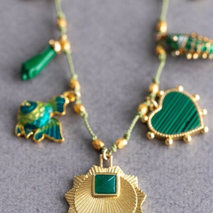 May include: A gold necklace with green gemstone charms. The charms include a heart, a fish, a star, and a small green stick. The necklace is made of a thin, green cord.