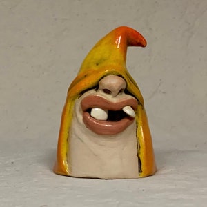 May include: A ceramic figurine of a character with a yellow and orange hat, a wide smile, and large teeth. The figurine is made in a whimsical style.