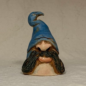 Può includere: Una piccola statuetta in ceramica di un gnomo con un cappello blu e un grosso baffo. Lo gnomo ha un'espressione capricciosa sul viso.