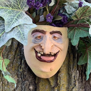May include: A whimsical planter shaped like a face with a wide smile and large, orange eyes. The planter is made of ceramic and is decorated with green and white ivy.