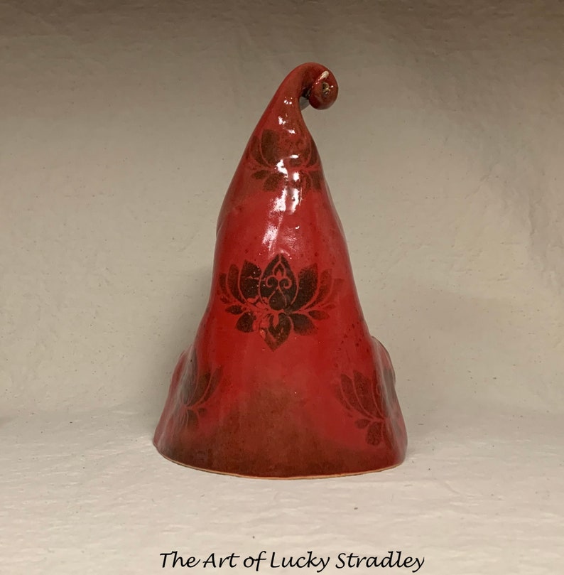 May include: A red ceramic sculpture with a lotus flower design. The sculpture is shaped like a hat with a curled top.
