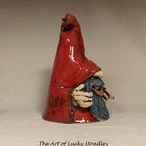 May include: A ceramic gnome figurine with a red pointed hat and a blue beard. The gnome is holding a small object in its hands.