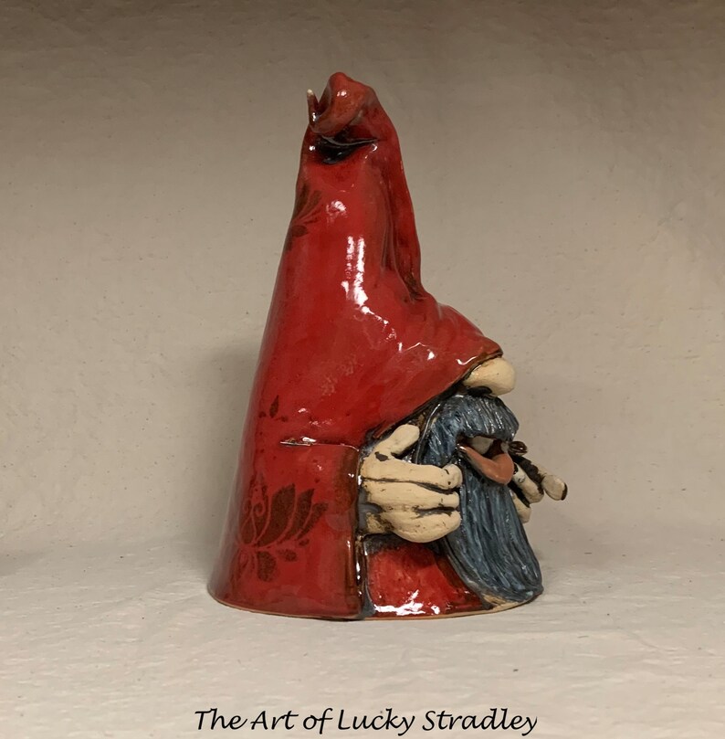 May include: A ceramic gnome figurine with a red pointed hat and a blue beard. The gnome is holding a small object in its hands.