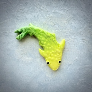May include: A ceramic fish figurine in shades of yellow and green. The fish has a textured body, a pointed tail, and small black eyes. The figurine is a decorative item.