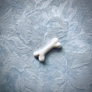 May include: A white ceramic dog bone on a blue textured background.