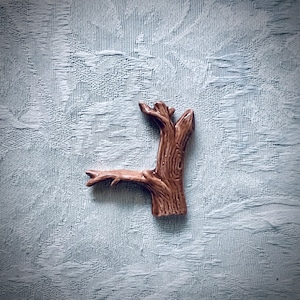 May include: A brown ceramic tree branch with detailed wood grain texture. The decorative piece has a small, angled branch extending to the left. The tree branch is a unique home decor accent.