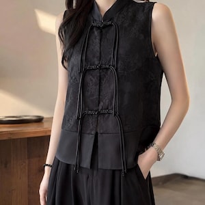 Peut inclure: Un haut noir sans manches doté d'un col officier et d'un motif floral jacquard ton sur ton. Le vêtement est agrémenté de trois fermetures brandebourgs noires verticales sur le devant et d'un panneau d'ourlet noir uni, créant une silhouette structurée.