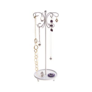 May include: White metal jewelry stand with a tree-like design. The stand has multiple hooks for hanging necklaces and earrings. There are several necklaces and earrings hanging from the stand.