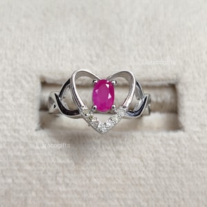 Peut inclure: Une bague argentée avec une pierre précieuse rose vif de taille ovale au centre, sertie dans un cadre en forme de cœur. La partie inférieure du cœur est ornée de petites pierres claires et l'anneau présente un motif ajouré en infini.