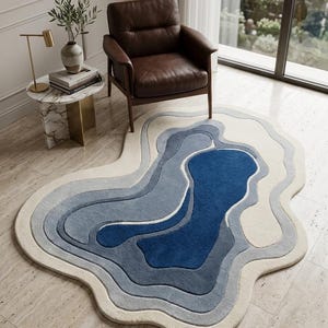 Può includere: Un tappeto di forma organica e irregolare con motivi concentrici a strati nei toni del crema, azzurro, blu ardesia e blu navy profondo. Il tappeto presenta una consistenza trapuntata con bordi distinti e rialzati dal design topografico.