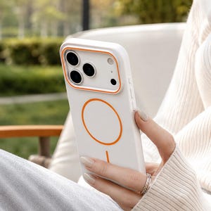 May include: A white smartphone case featuring a bright orange circular magnetic charging ring on the back and a matching orange rectangular frame surrounding the camera lens cutout. The case has a smooth matte finish and a slim profile design.